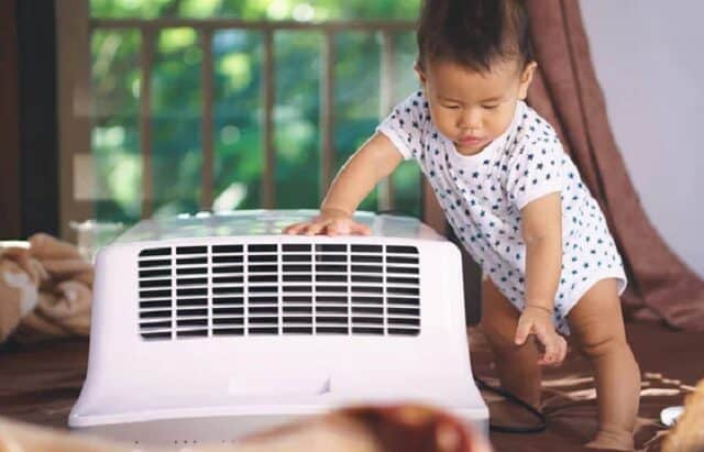 un bebe regarde un climatiseur mobile